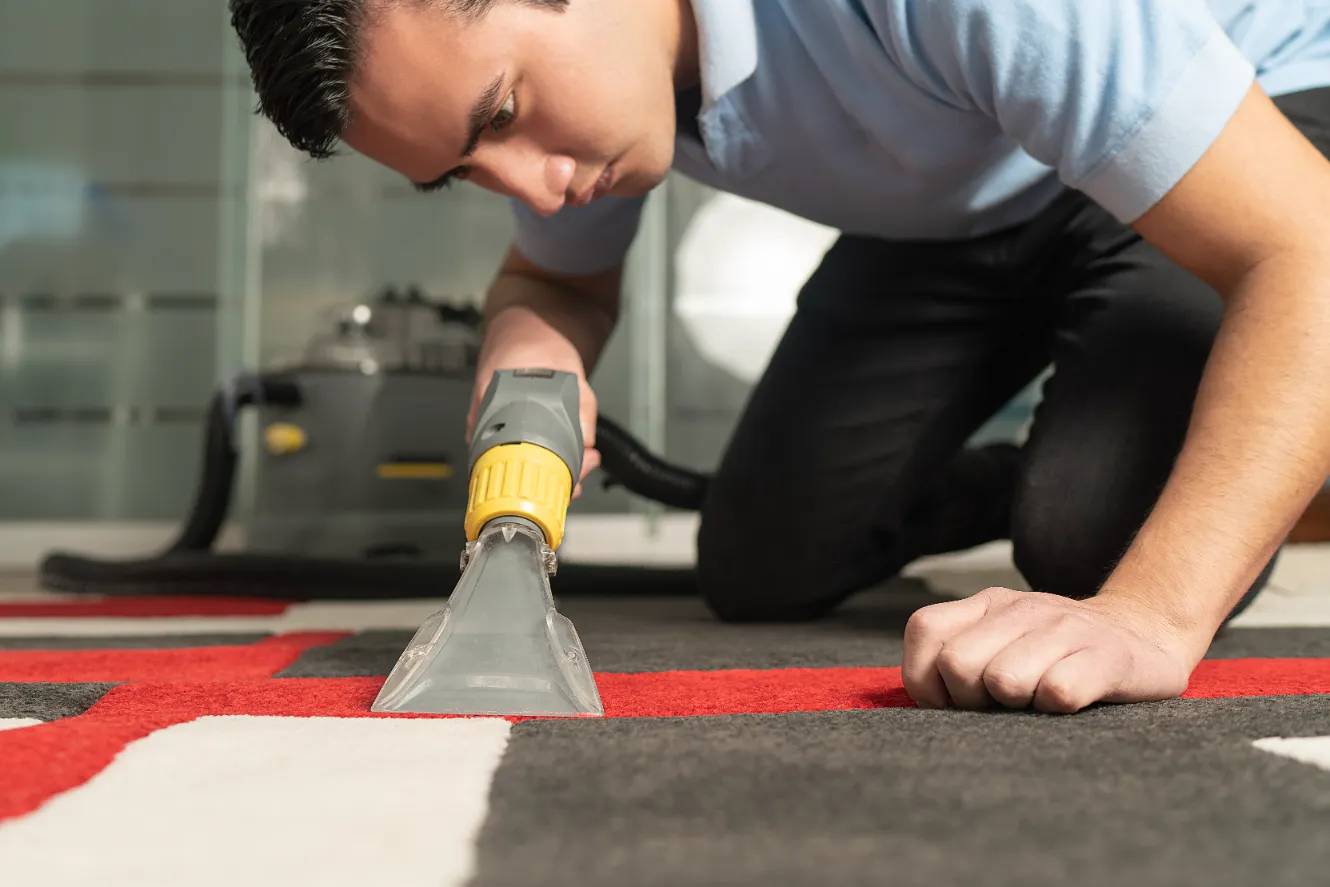 A man carefully removing the stains and dirt on the carpet using a vacuum cleaner.