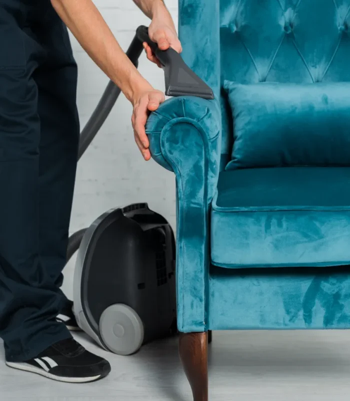 A service worker cleaning the sofa chair with a vacuum cleaner.